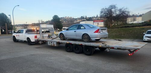 Flat deck trailer towing a blue car in Kamloops