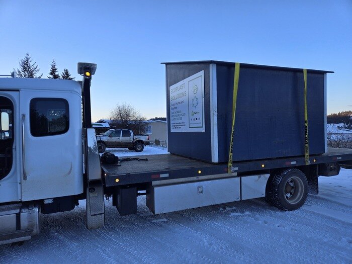 Phil's Towing flat deck truck hauling a shed strapped down to the deck
